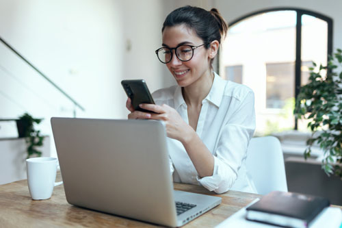 Smiling business woman using her mobile phone while working with computer in the office.